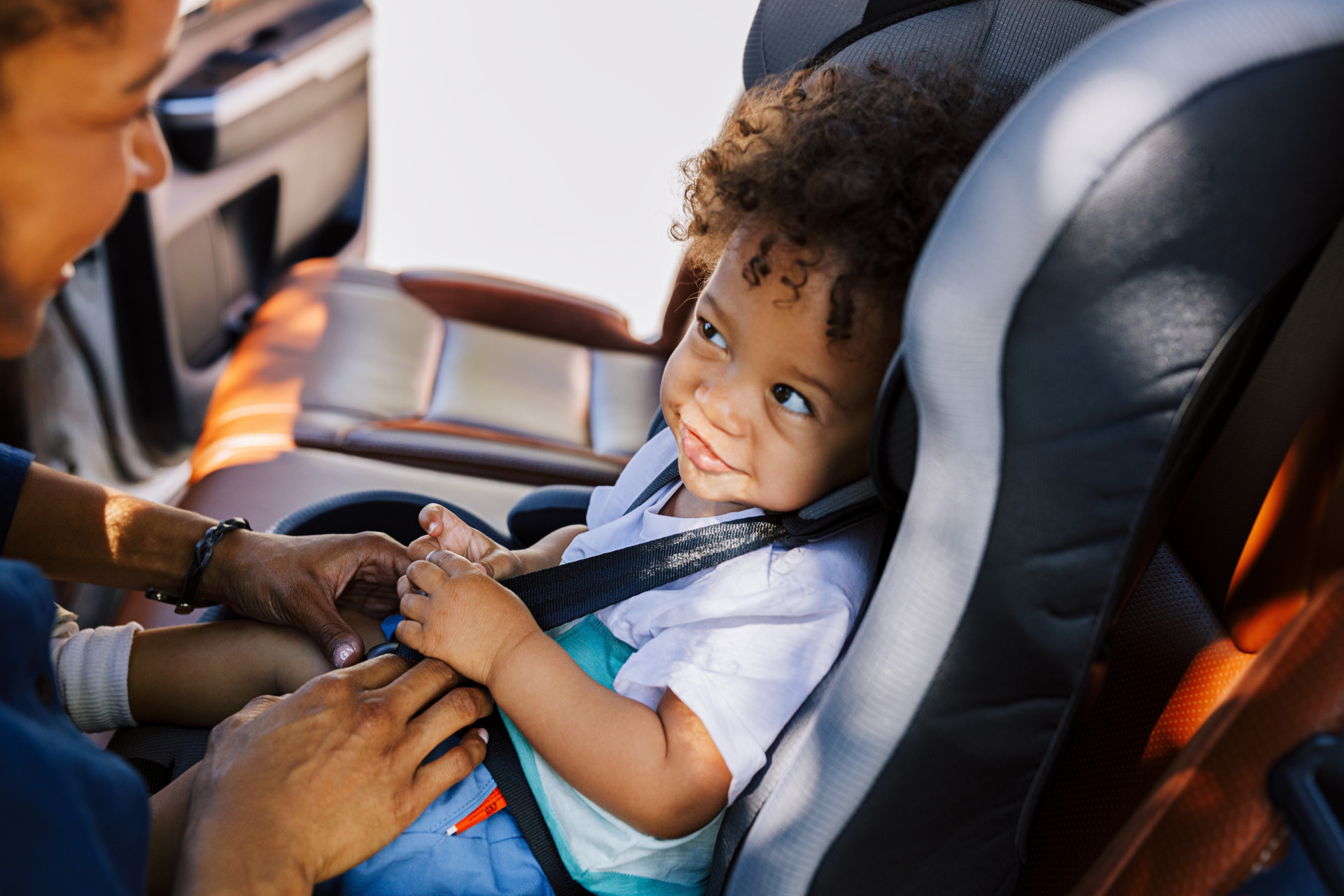 Mother Adjusting Car Seat Straps for her toddler son in the back seat of her car