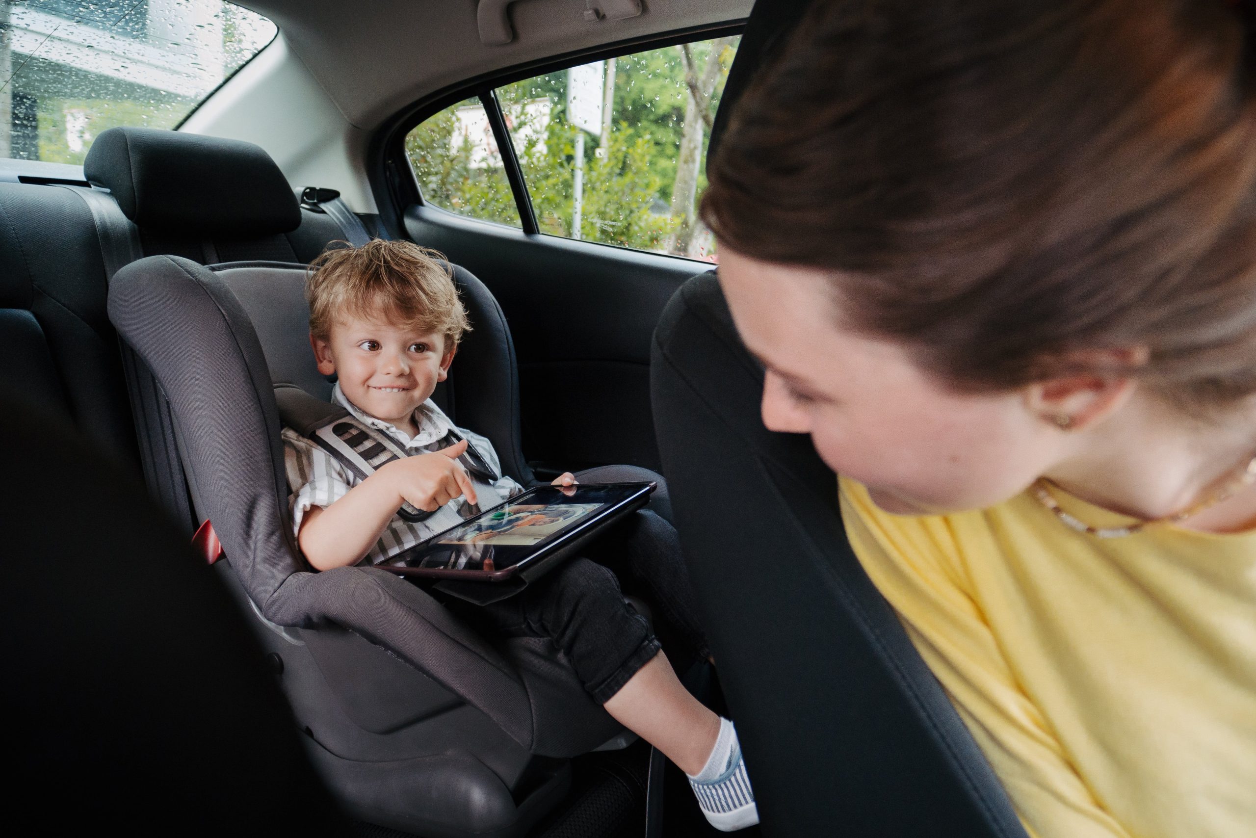 child in the backseat of a car playing on his tablet