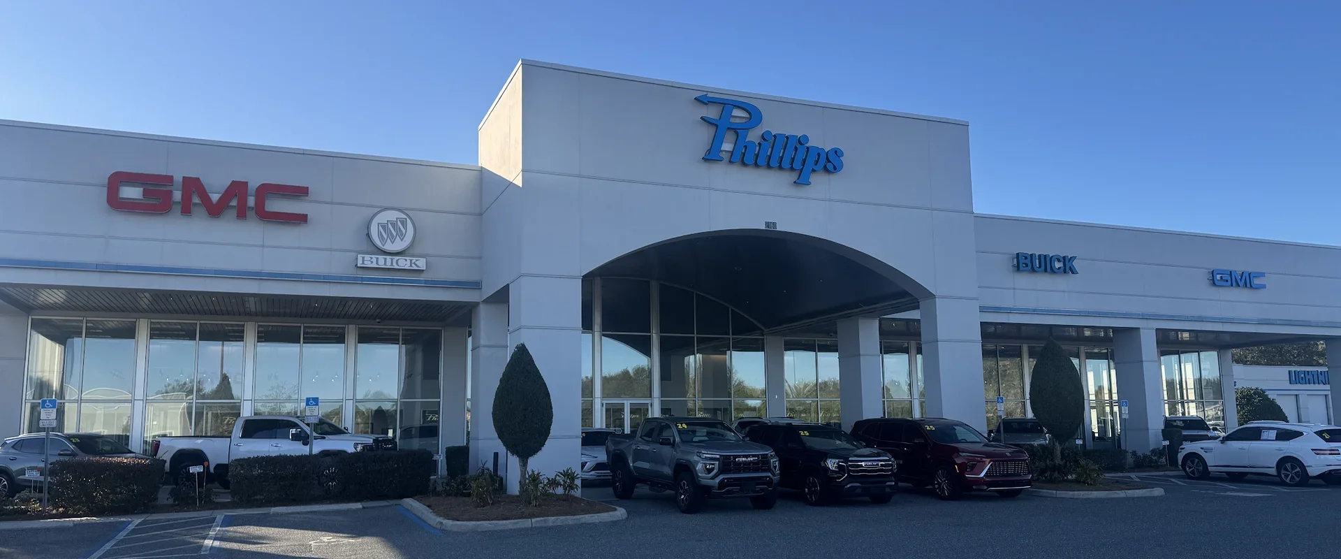 The Phillips Buick GMC showroom in Fruitland Park, FL, with GMC and Buick signs on the building and new GMC and Buick vehicles parked out front