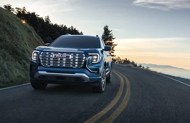 A blue GMC Terrain Denali driving along a winding coastal road at sunset