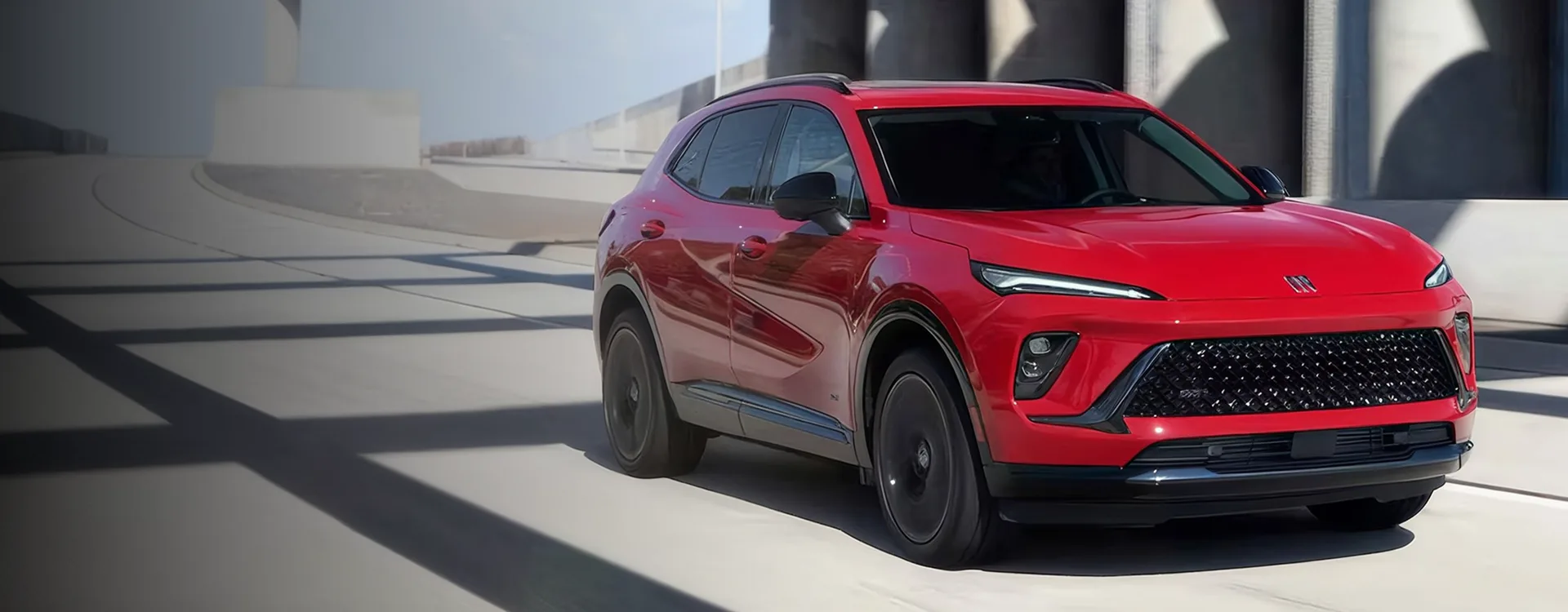 Red 2026 Buick Envision driving out of a concrete parking structure, seen from the front three-quarter angle