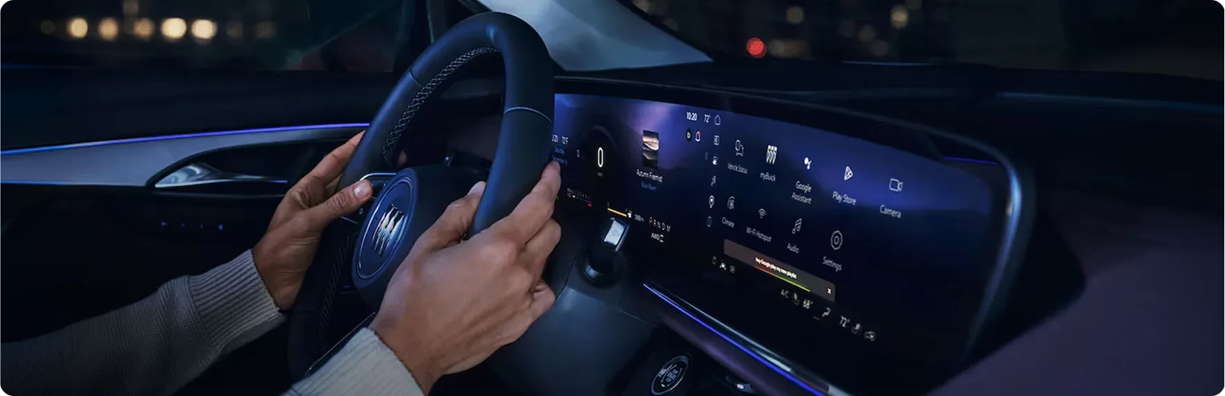 Driver's hands on the Buick Envision steering wheel at night with city lights through the windshield