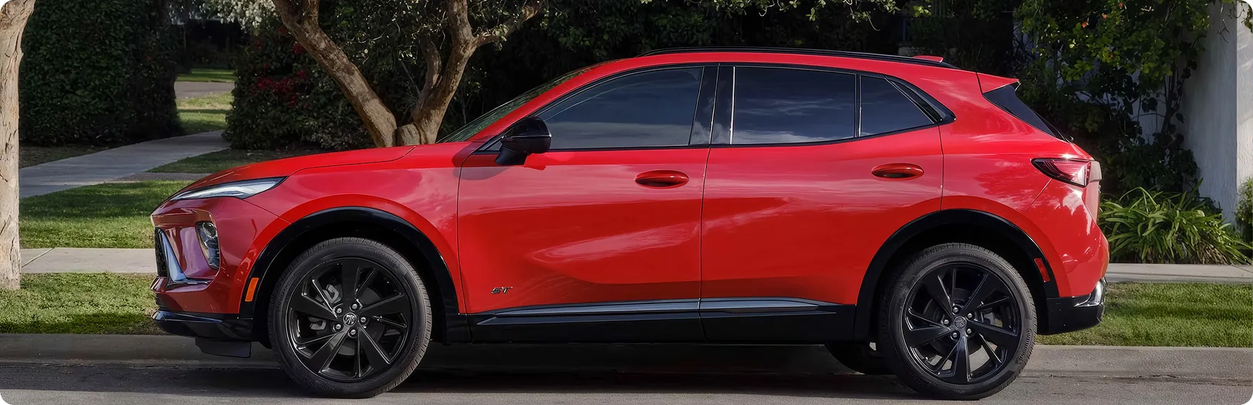 Red Buick Envision parked in a driveway lined with trees, seen from the side