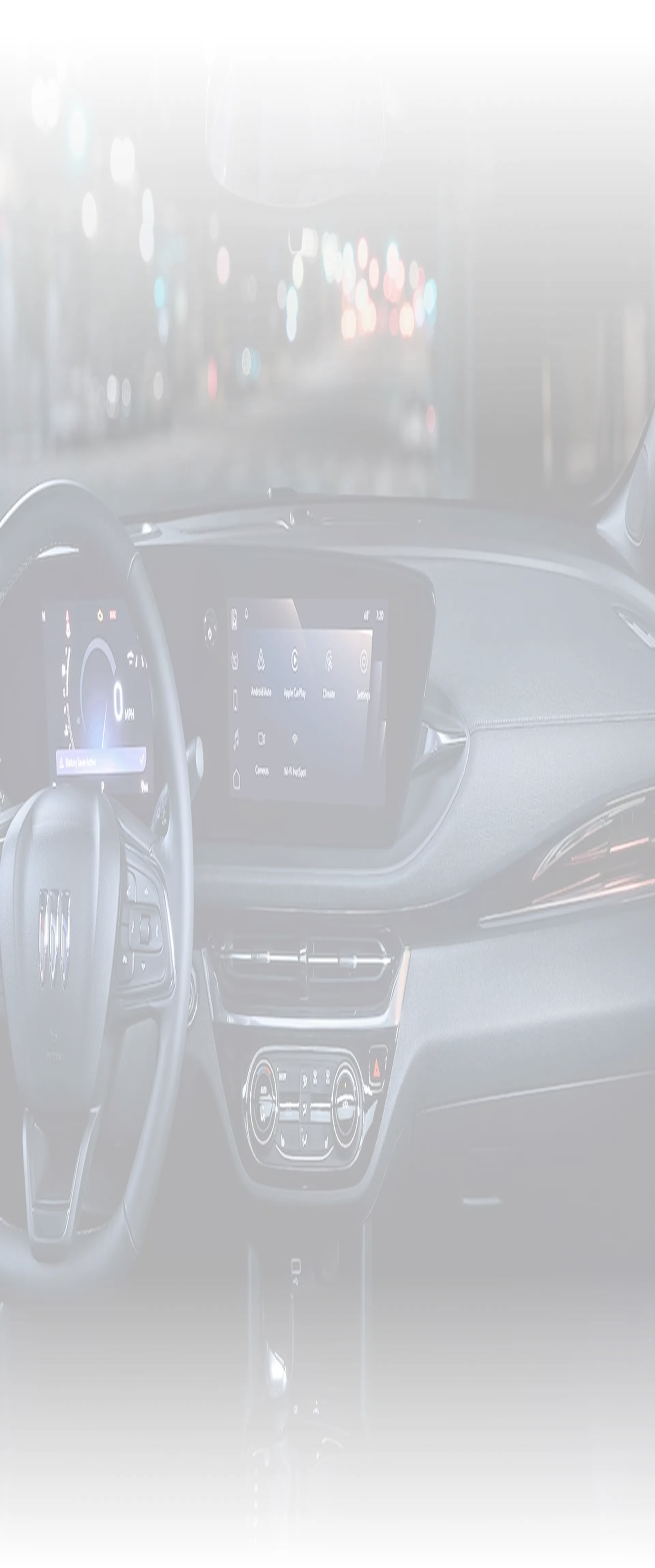 The Buick Envision cockpit at night with the steering wheel and ultrawide display lit against city lights