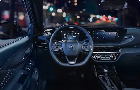 Buick Envista steering wheel and infotainment display lit at night with city lights beyond the windshield