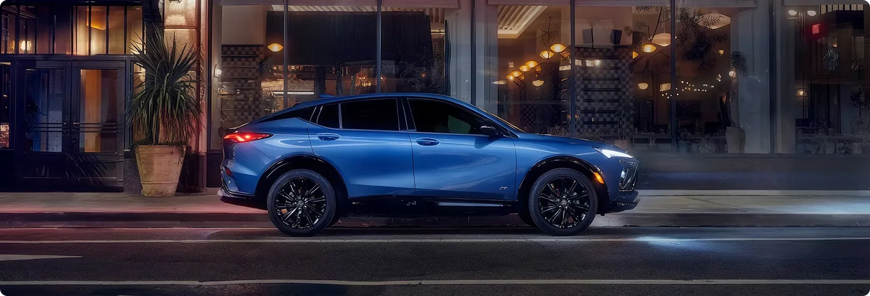 Blue Buick Envista parked in profile outside a lit storefront at night