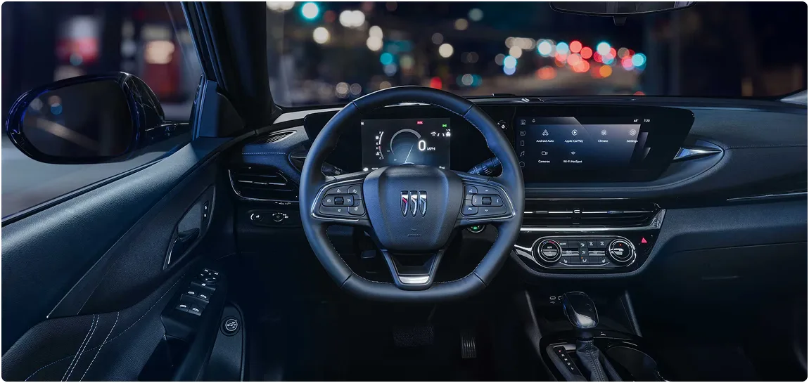 Buick Envista steering wheel and infotainment display lit at night with city lights beyond the windshield
