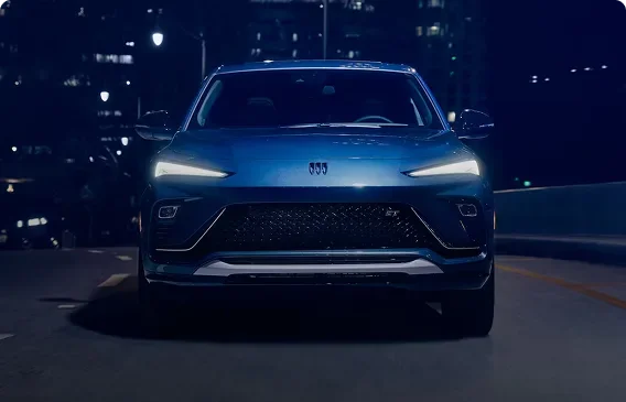 Blue Buick Envista Sport Touring seen head-on at night, showing its gloss black mesh grille
