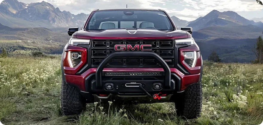 Red GMC Canyon AT4X seen head-on in a mountain meadow, showing its bold grille and brush guard