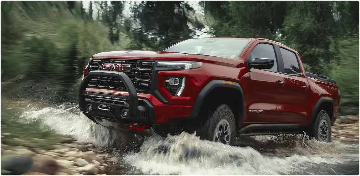 Red GMC Canyon AT4X powering through a river crossing, throwing up spray