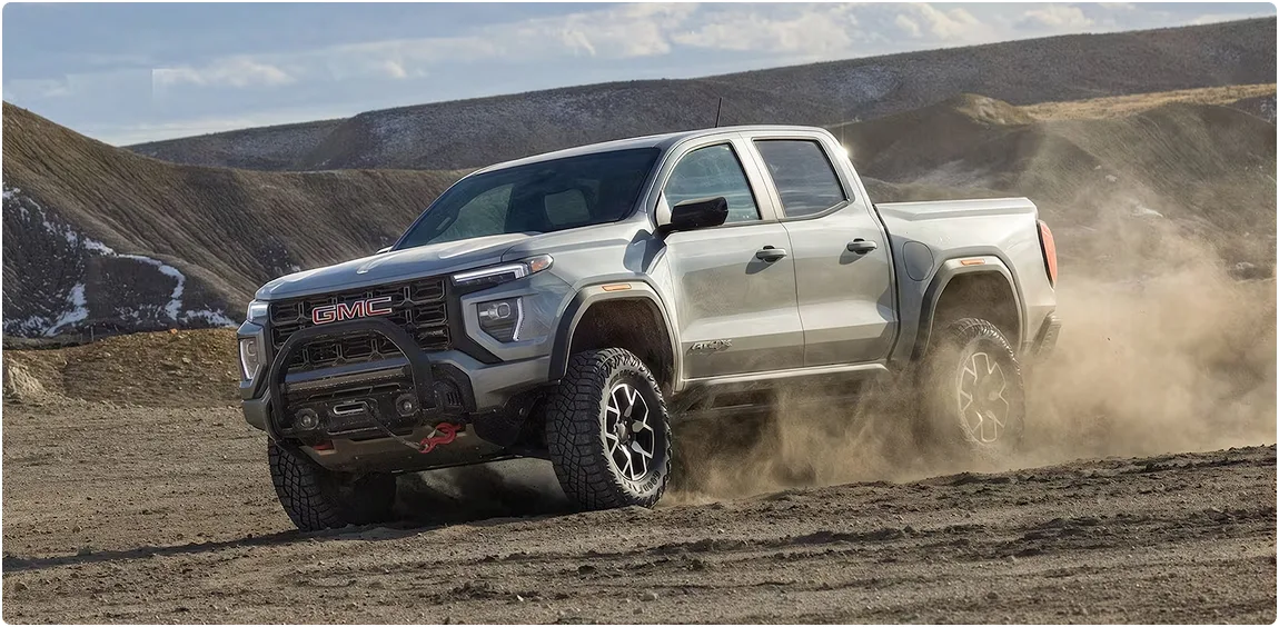 Silver GMC Canyon AT4X sliding across a dirt flat in a cloud of dust