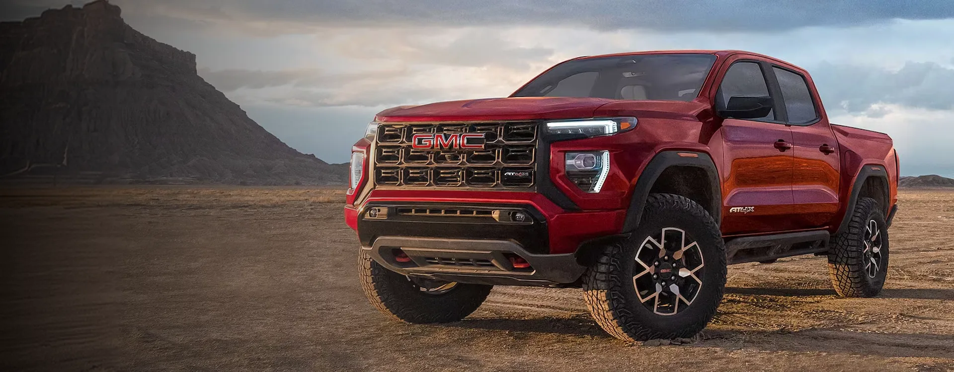 Red 2026 GMC Canyon AT4X parked on desert flats below a mesa, seen from the front three-quarter angle