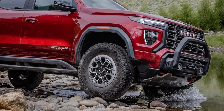 Red GMC Canyon AT4X crossing a rocky riverbed with its off-road suspension flexed