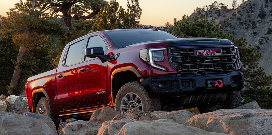 Red GMC Sierra 1500 AT4X climbing over rocks on a mountain trail