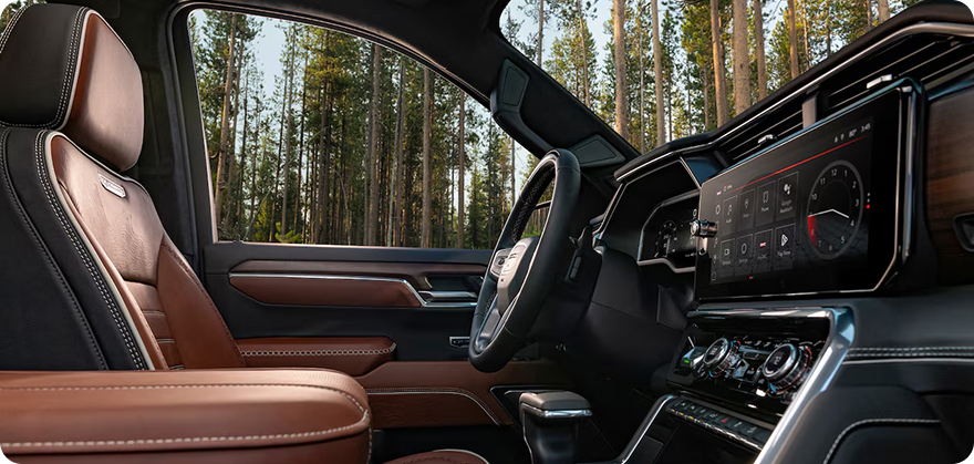 Brown leather front seat and wide touchscreen in the GMC Sierra 1500 Crew Cab, forest beyond the windows