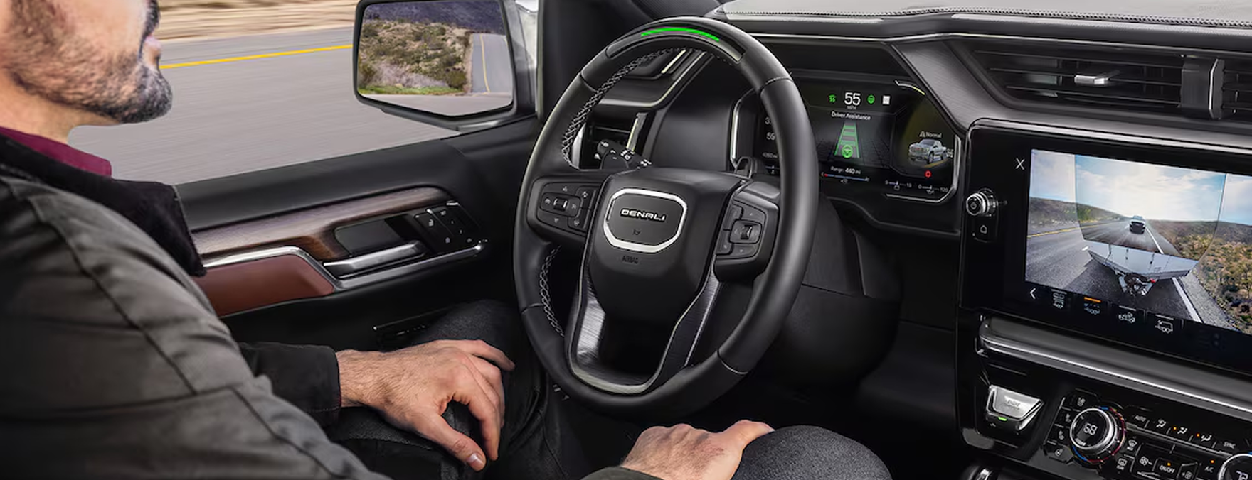 Driver with hands off the wheel using Super Cruise in a GMC Sierra 1500, the steering wheel light bar glowing green