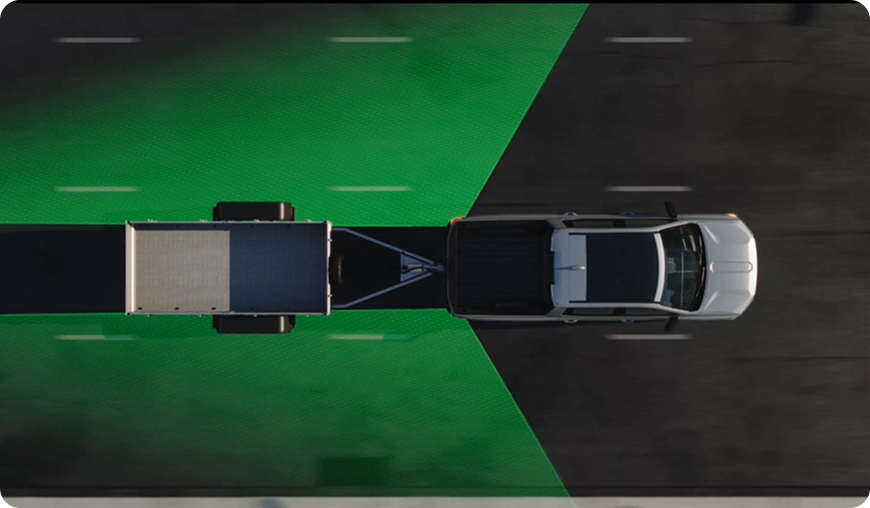 Overhead illustration of a GMC truck towing a flatbed trailer, with green blind zone areas extending along the trailer