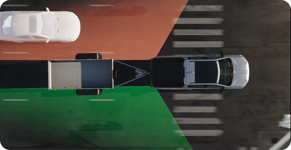 Overhead illustration of a GMC truck towing a trailer, with blind zone areas extended along the trailer and a car in the next lane