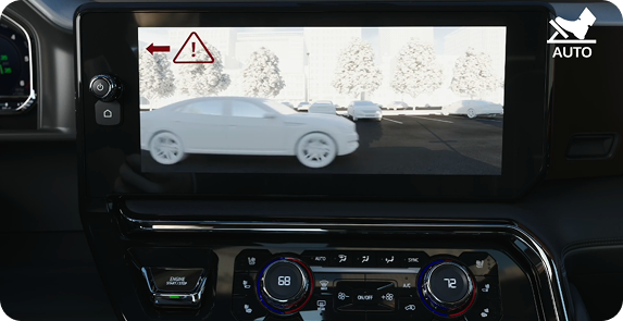 Center touchscreen showing a rear camera view of a passing car with a red warning triangle