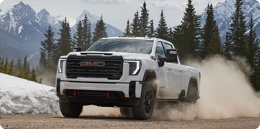 White GMC Sierra HD kicking up dust on a mountain road lined with pine trees