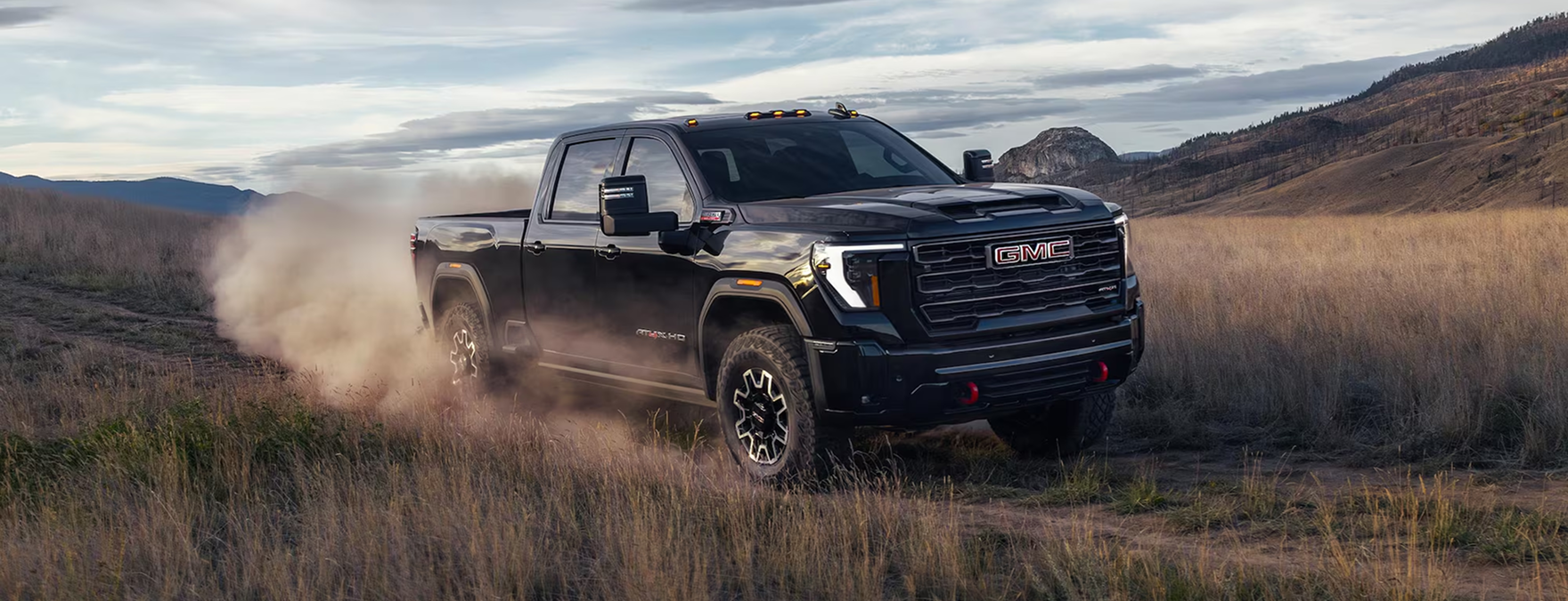 Black GMC Sierra HD driving across a grassy valley, trailing a cloud of dust