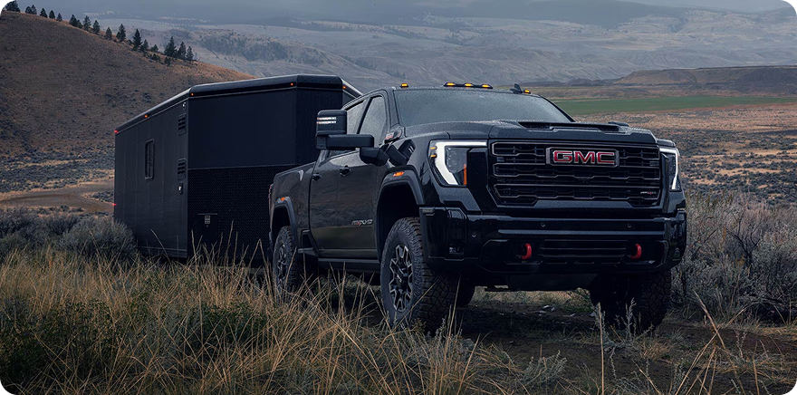 Black GMC Sierra HD towing a black off-road trailer through sagebrush hills