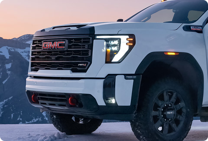 Close-up of the LED headlamp and grille on a white GMC Sierra HD AT4 parked in the snow at dusk