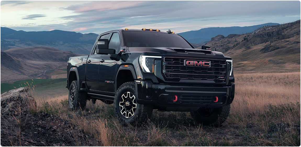 Black GMC Sierra HD parked on a grassy hillside at dusk with mountains behind