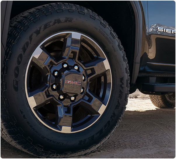 Close-up of a black machined-face wheel and Goodyear all-terrain tire on a GMC Sierra HD