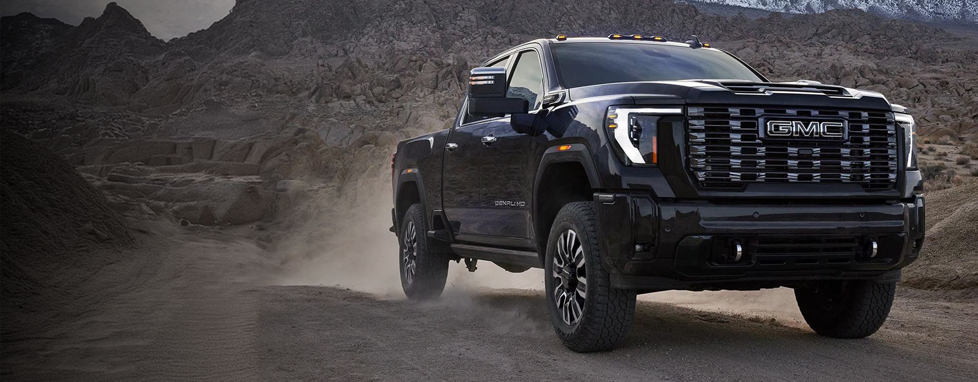 Black 2026 GMC Sierra 2500 HD Denali kicking up dust on a desert trail, seen from the front three-quarter angle