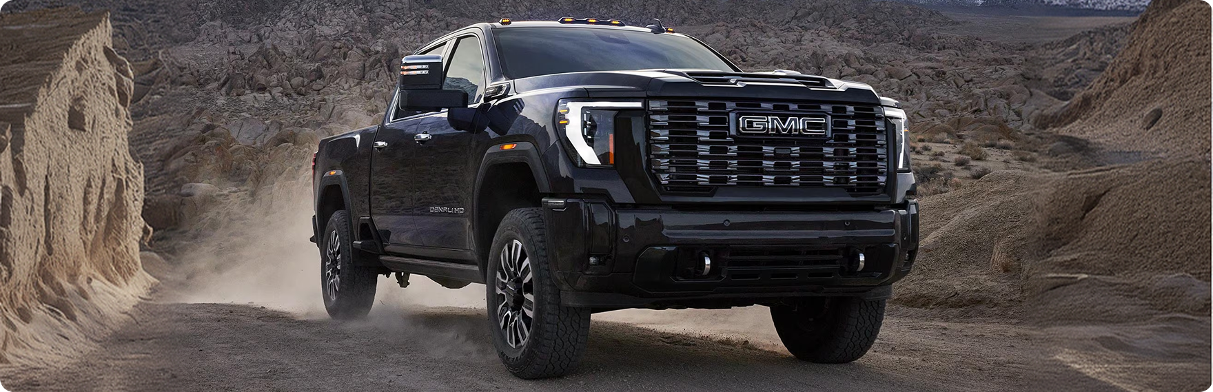 Black GMC Sierra HD Denali driving between sandstone formations on a dusty desert trail