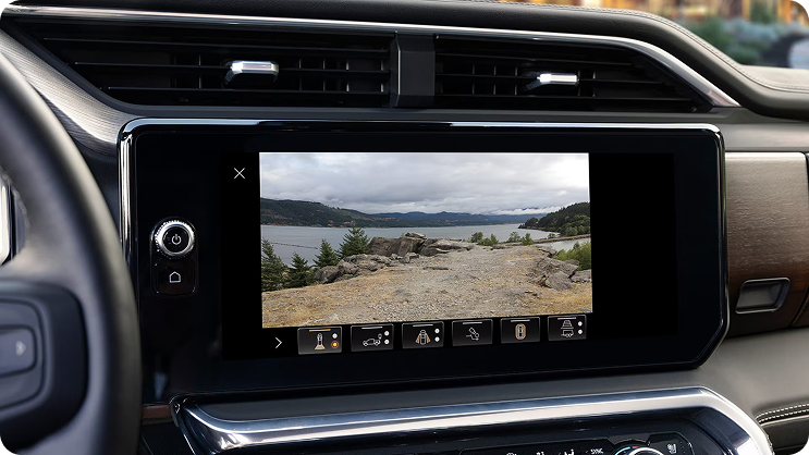 Center touchscreen showing a rear camera view of a gravel lot beside a lake