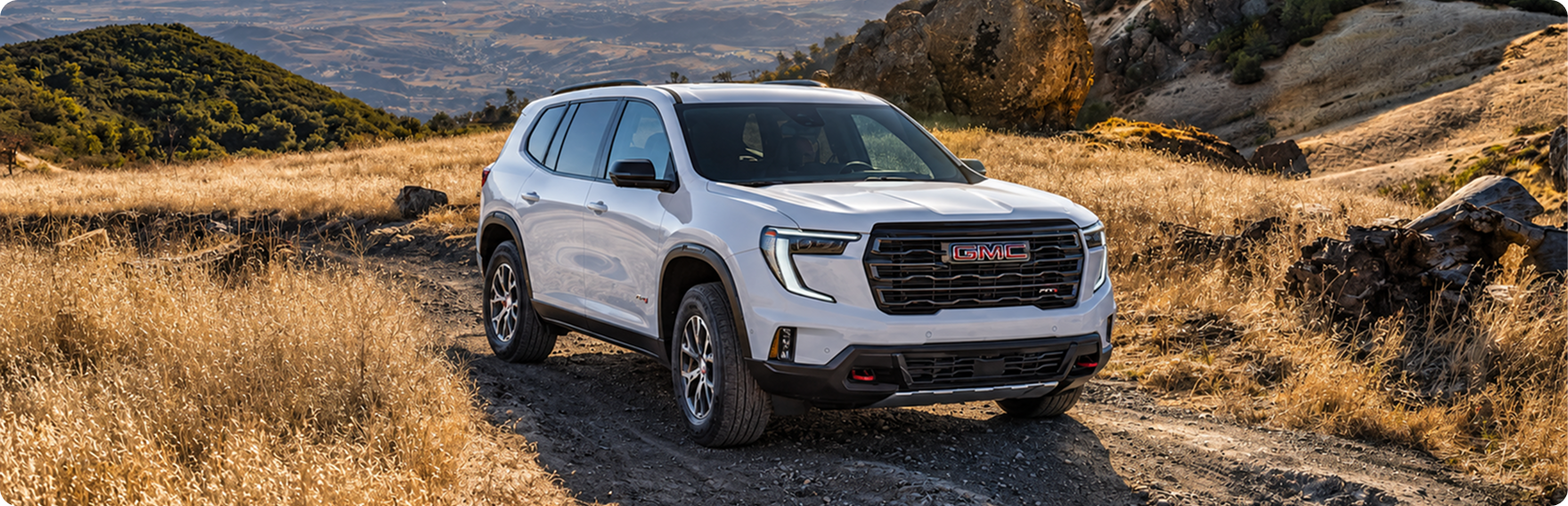 White GMC Acadia AT4 driving a dirt trail through dry grass hills