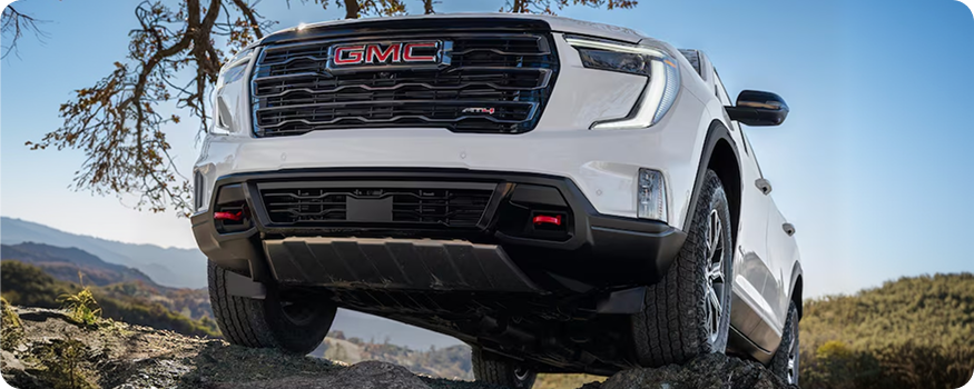 Low-angle front view of a white GMC Acadia AT4 climbing over rocks