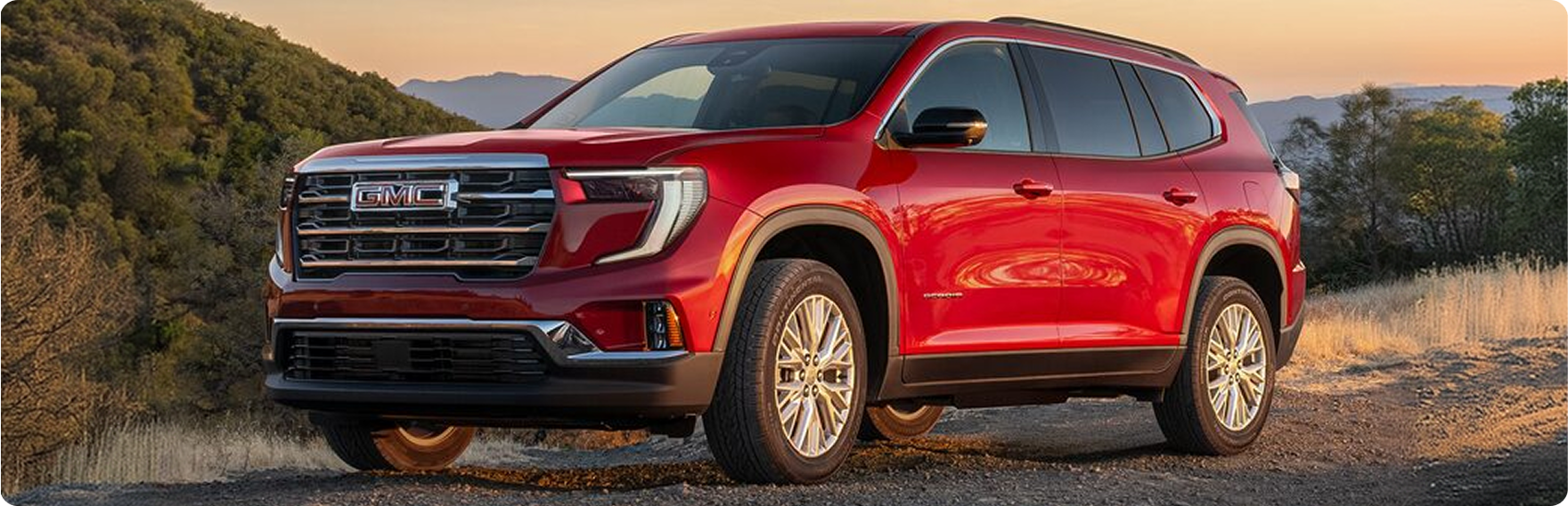Red GMC Acadia parked on a hillside trail at sunset, seen from the front three-quarter angle