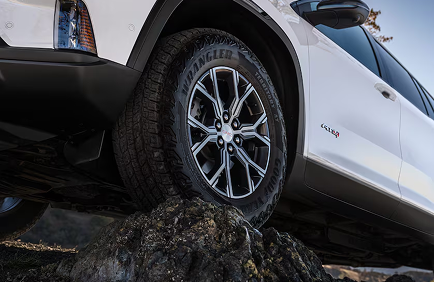 Front wheel of a white GMC Acadia AT4 with an all-terrain tire resting on a rock