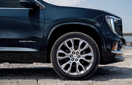 Front fender of a dark blue GMC Acadia Denali with Denali badging and a machined aluminum wheel