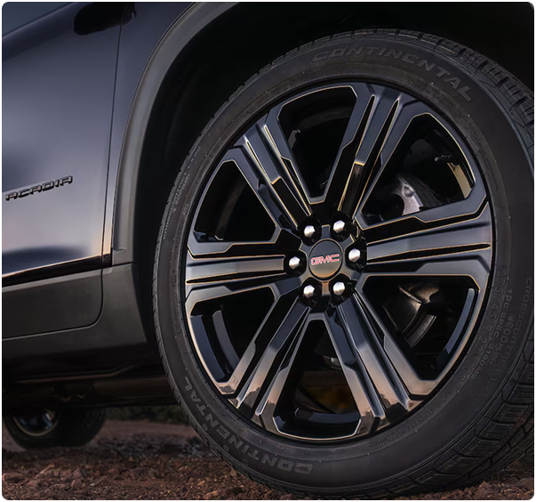 Close-up of a dark multi-spoke GMC Acadia wheel with a GMC center cap