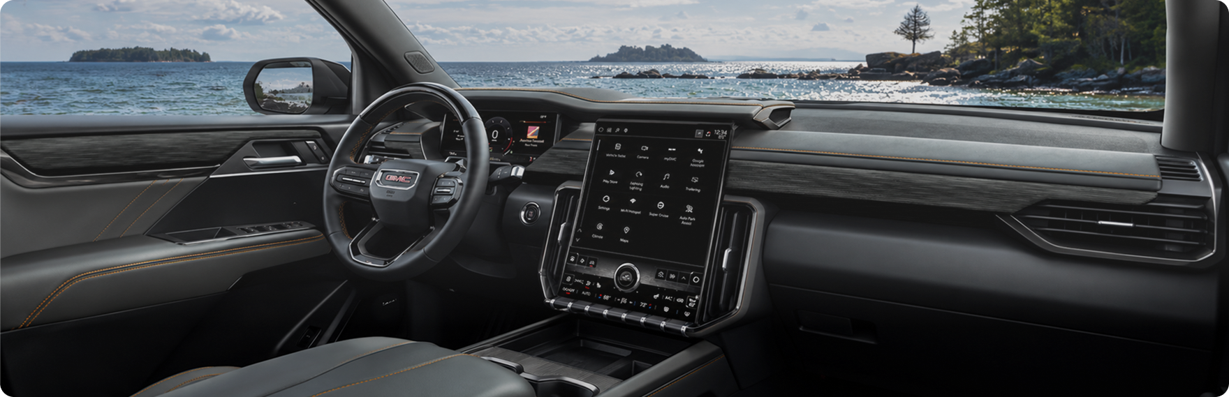 GMC Acadia cabin with the steering wheel and portrait center touchscreen, a lake visible through the windshield