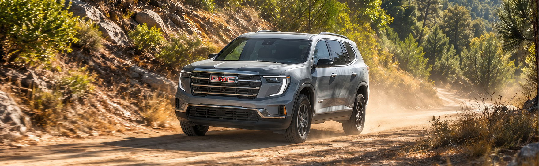 Gray GMC Acadia kicking up dust on a forest dirt road