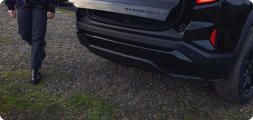 A person walking up to the rear of a 2027 GMC Terrain Elevation as the power liftgate opens