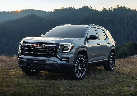 Blue-grey 2027 GMC Terrain Elevation in a mountain meadow, seen from the front three-quarter angle