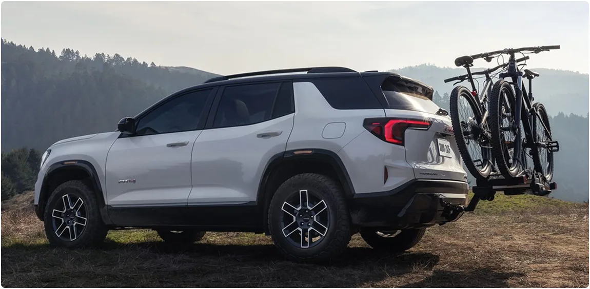 White 2027 GMC Terrain on a mountain ridge with two bikes on a hitch-mounted rack