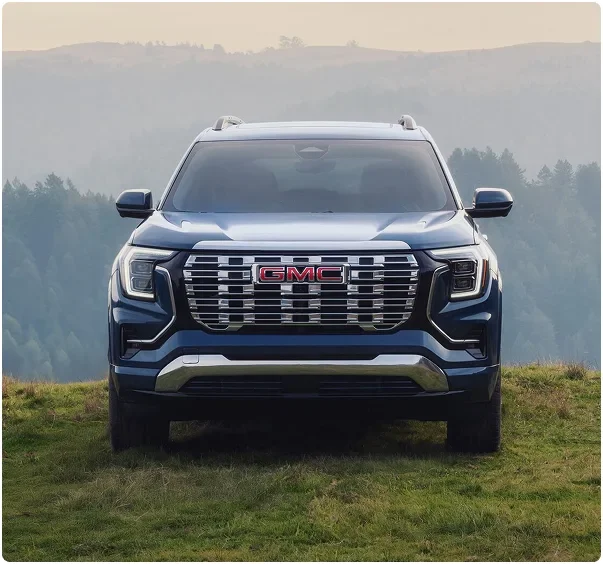 Blue 2027 GMC Terrain Denali seen head-on in a grassy mountain clearing