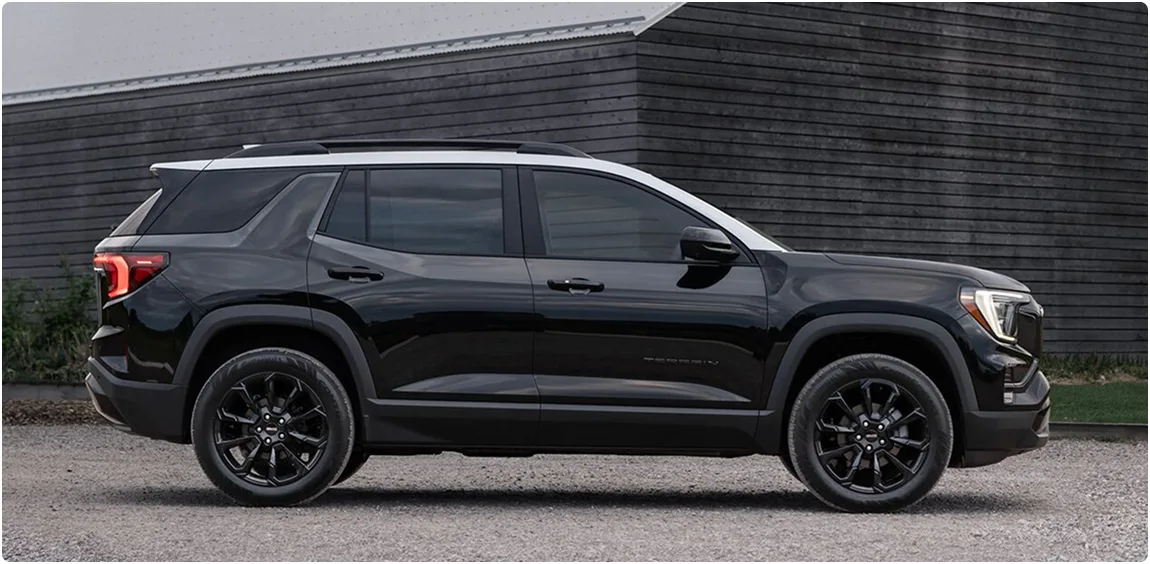 Black 2027 GMC Terrain parked in profile beside a dark barn