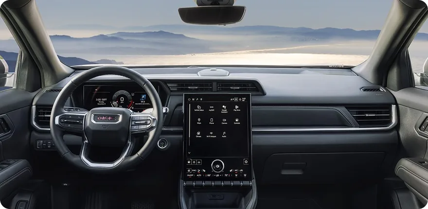 Full-width view of the 2027 GMC Terrain's dashboard, steering wheel and infotainment touchscreen with a mountain lake beyond the windshield