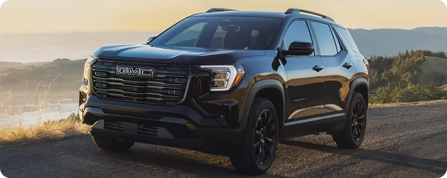 Black 2027 GMC Terrain on a gravel overlook above a valley at sunrise