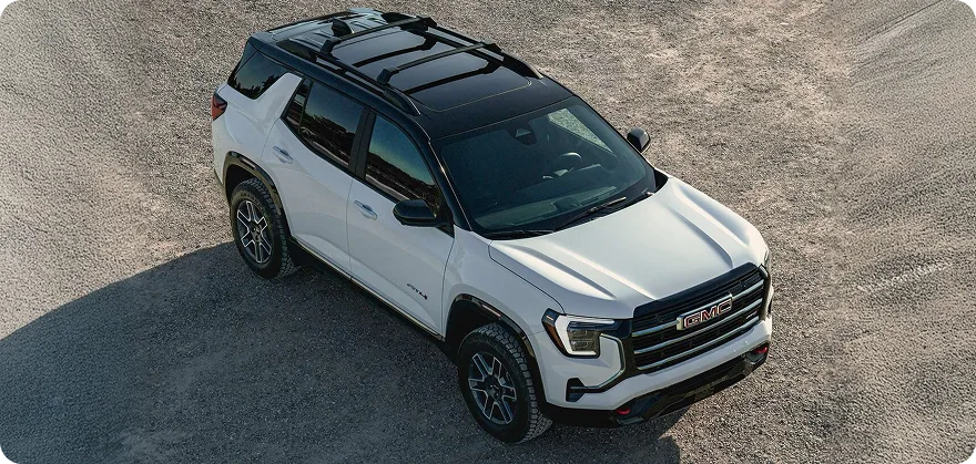 High-angle view of a white 2027 GMC Terrain with a black two-tone roof on a gravel clearing