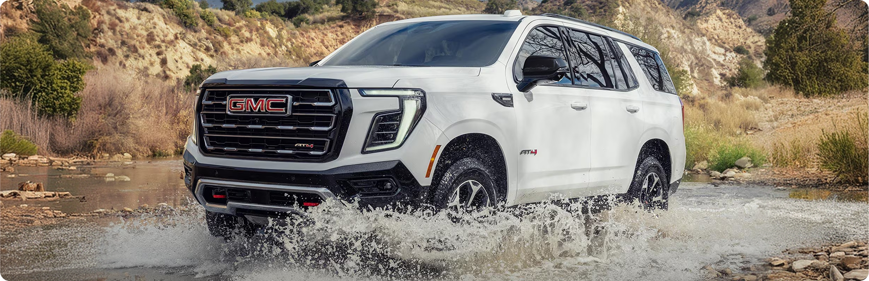 White GMC Yukon AT4 splashing through a shallow stream