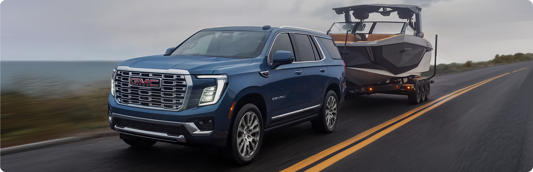 Blue GMC Yukon Denali towing a boat along a coastal highway